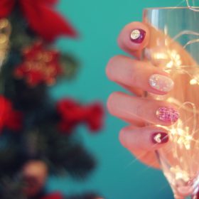 クリスマスツリーとシャンパングラスを持つ女性の手元