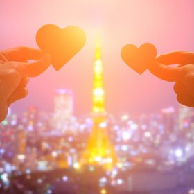 夕日に照らされた東京タワーで、愛のハートの紙を握るロマンチックな恋人たちのシルエット