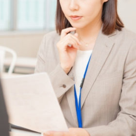 書類を見ながらお客様に対応するベージュ色のスーツの女性