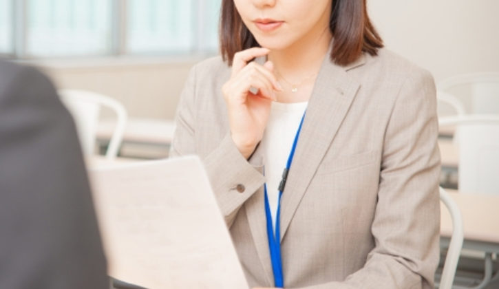 書類を見ながらお客様に対応するベージュ色のスーツの女性