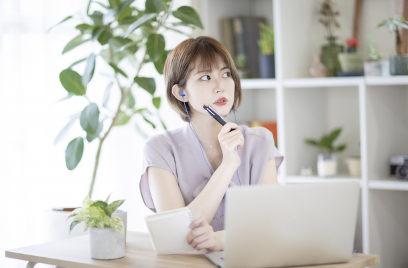 ノートパソコンの前で天井を見つめながら考え事をする女性