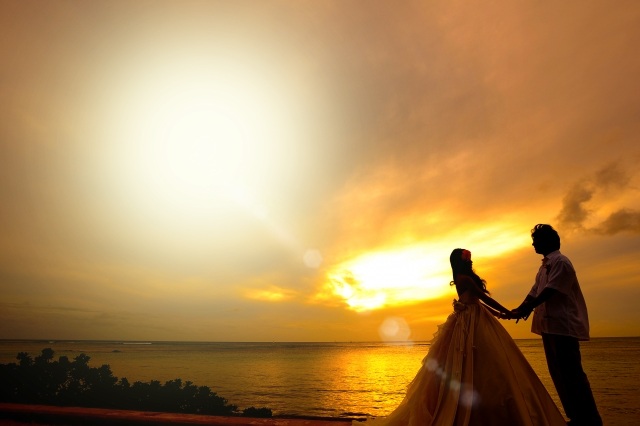 夕焼けの海岸で手を取り合うウェディングとタキシード姿のカップル