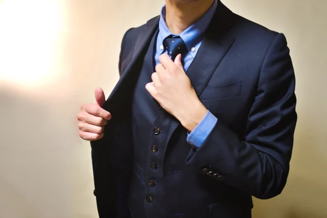 紺色のネクタイとスリーピーススーツに青いシャツを着た男性