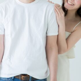 白いTシャツとジーパンを着た男性の肩の後ろから笑顔でを近づける白いキャミソールの女性