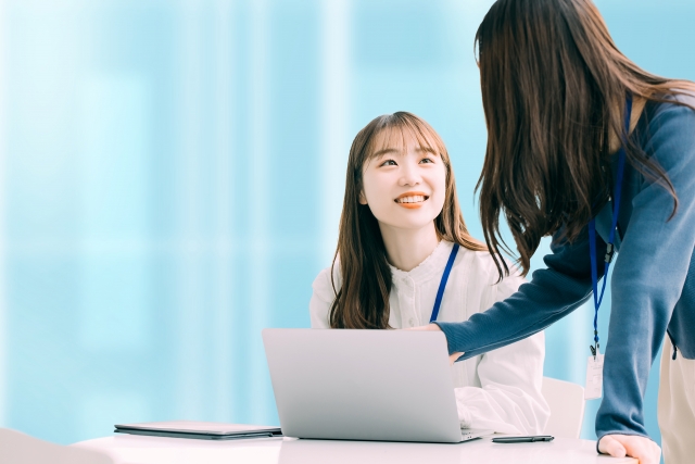 ノートプックパソコンを使っている女性の横に立ってアドバイスをする女性