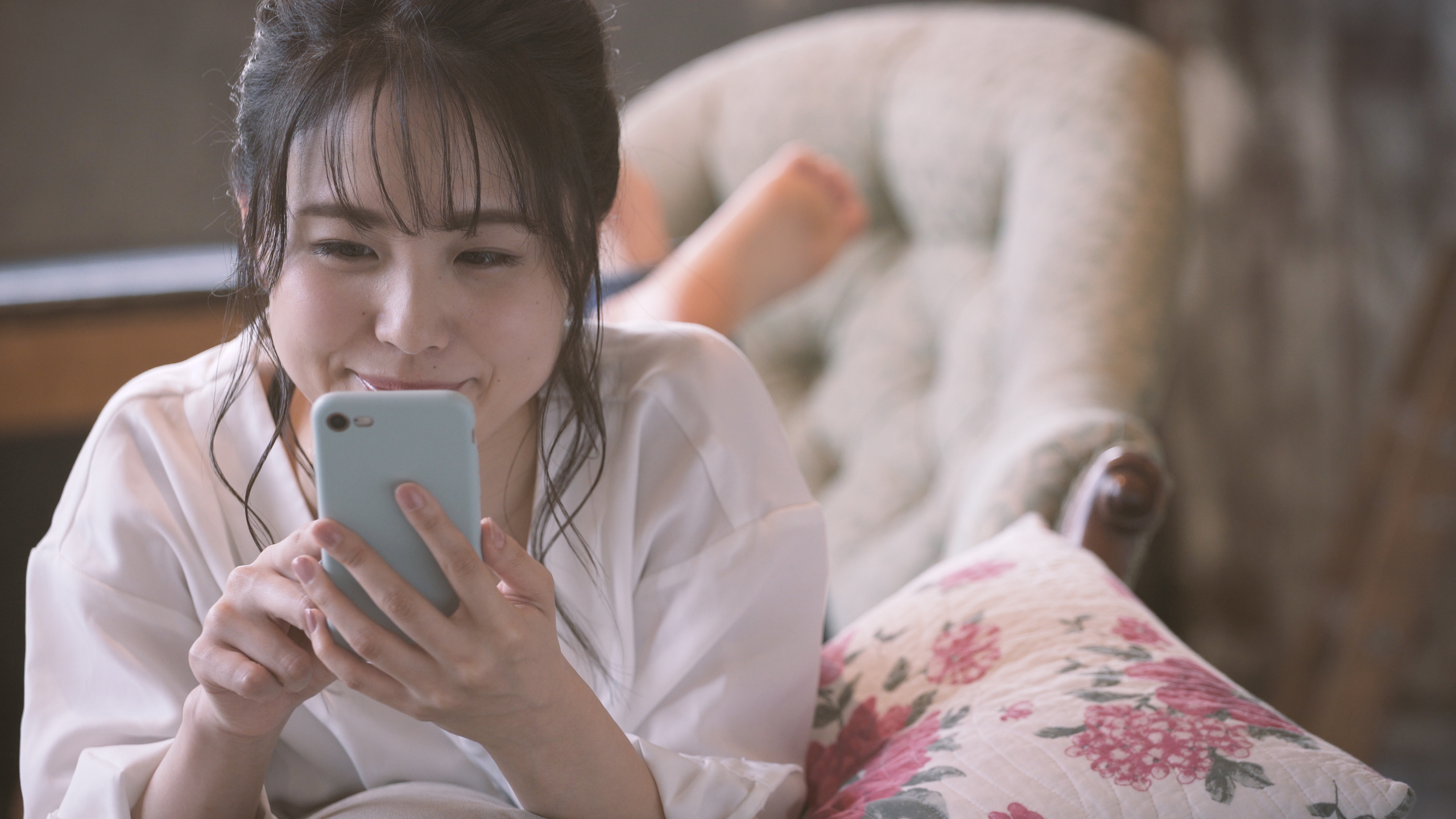 自宅のベットでうつ伏せになってスマホを操作する笑顔の女性