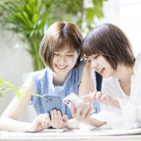 お互いの携帯を見せ合う2人の30代女性