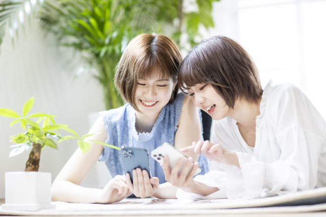 お互いの携帯を見せ合う2人の30代女性